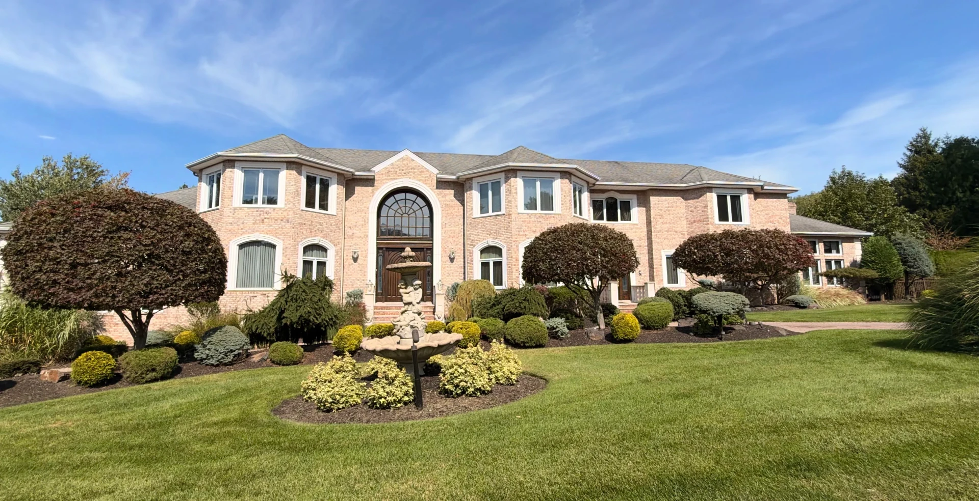 Large brick estate with a stone fountain in the front garden
